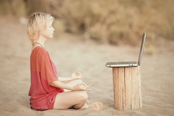 Girl blonde teenager in red blouse meditating in front of a laptop at the beach