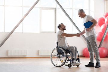 Cheerful disabled patient greeting his physical therapist in the gym