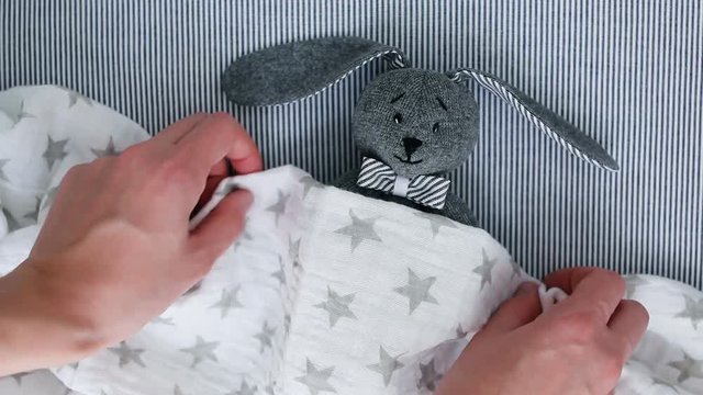 Mom lays a soft toy with a blanket in a baby round crib