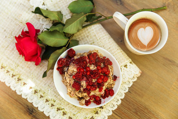 Plate with porrige,cup with coffe and red rose on the rough table napkin.Wooden table background.