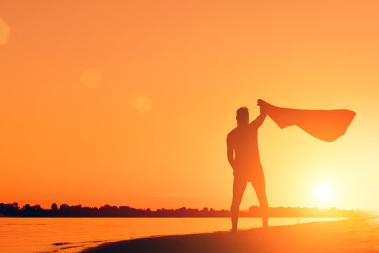 Silhouette of a naked man with a towel on the beach at sunset