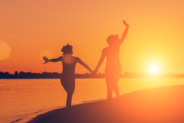 Silhouette of a woman holding hands running on the beach at sunset