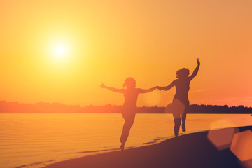 Fototapeta premium Silhouette of a woman holding hands running on the beach at sunset