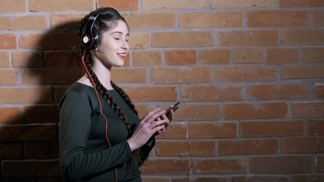 Woman in earphones listen music at brick wall in dark room