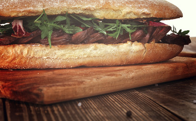 Sandwich with beef steak on a wooden stand.