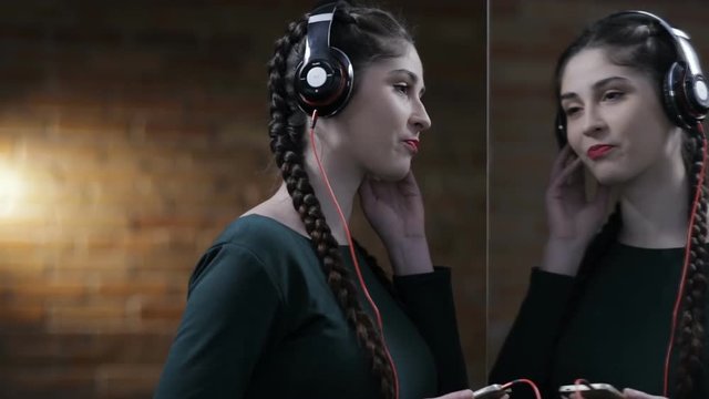 Woman in earphones listen music at mirror in dark room