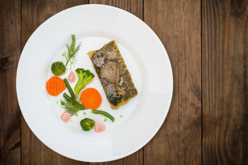 Tasty baked fish on plate on table close-up. Wooden background. Top view. Close-up