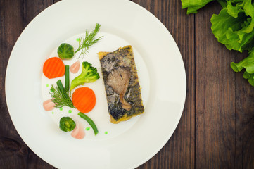 Tasty baked fish on plate on table close-up. Wooden background. Top view. Close-up