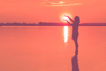 Woman is holding sun  in water at sunset