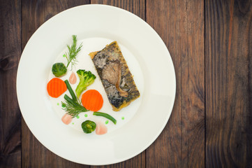 Tasty baked fish on plate on table close-up. Wooden background. Top view. Close-up