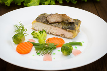 Tasty baked fish on plate on table close-up. Wooden background. Top view. Close-up