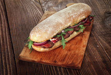 Sandwich with beef steak on a wooden stand.