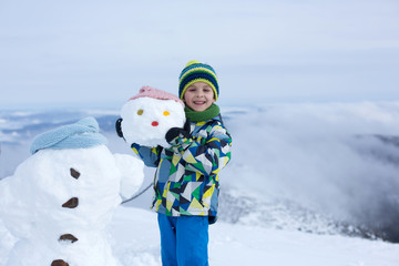Cute child, building snowman and playing with it on top of mount