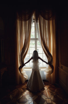 The charming bride stands near window in the restaurant