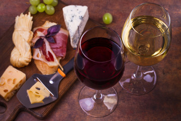 Glasses of red and white wine with smoked cheese, grape, prosciutto, garlic and bread. Wine and cheese still life. Food and drinks concept