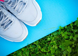 Sneakers and yoga mat on fresh green grass. Sports in the open air