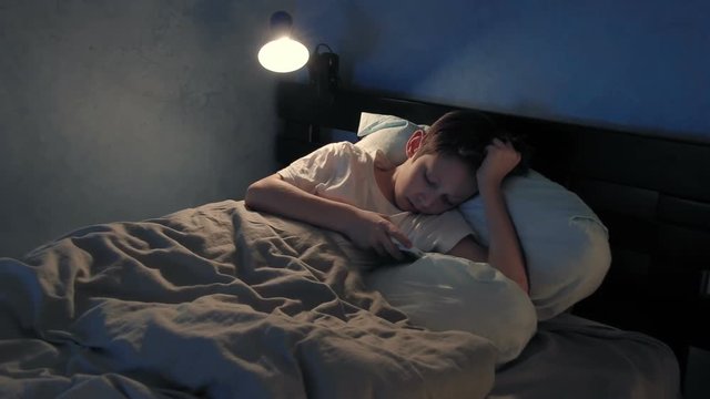 Boy resting in his bed in the evening and using his smart phone