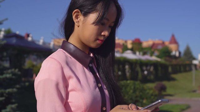 Portrait young asian woman using app on smart phone. Attractive female standing on the street and texting message.