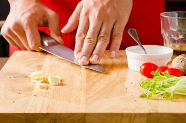 Chef slightly crushed garlic by knife on wooden board