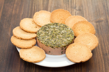 pate with toasts on white plate on brown wooden background