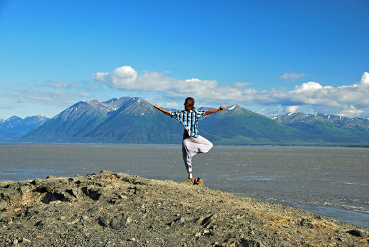 Man doing yoga at the coastline facing the mountains at Turnagain Arm in Alaska