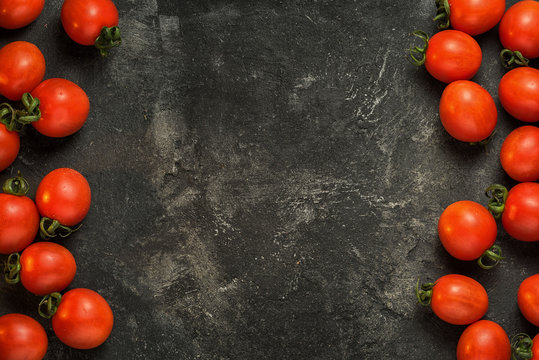 sided food frame of cherry tomatoes on a dark black stone cement background with copy space in the middle