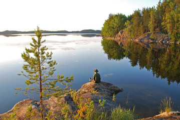 Man sitting at still Saimaa lake in Finland at sunset 