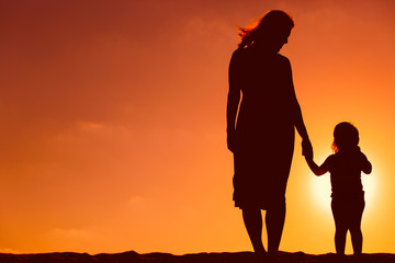 silhouette of mother and daughter holding hands at sunset