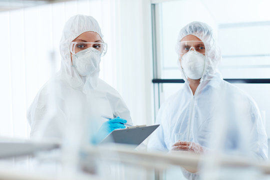 Two colleagues in overalls, eyeglasses, gloves and respirators working in lab