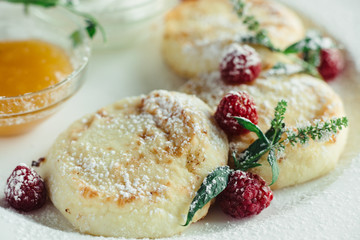 cheese pancakes with raspberries and honey on a white plate on a wooden table