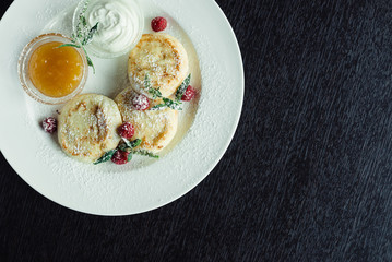 cheese pancakes with raspberries and honey on a white plate on a wooden table