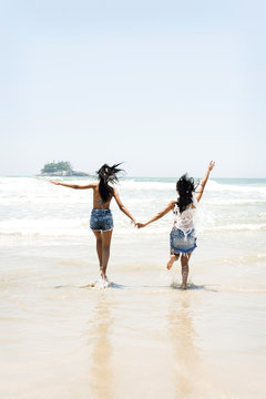 Brazil, Sao Paulo, Ubatuba, two young women running on the beach holding hands