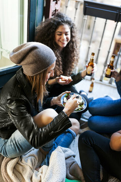 Group of friends sitting on the floor eating pizza and salad and drinking beer at home
