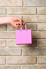 pink shopping bag in female hand on brick wall