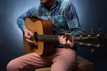 Young man playing on acoustic guitar close up