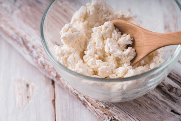Fresh soft cheese in the glass bowl on the white wooden table horizontal