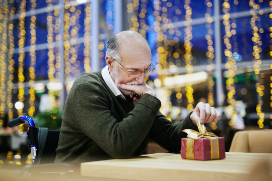 Disabled senior man looking at gift-box on table
