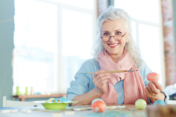 Grey-haired woman painting Easter eggs