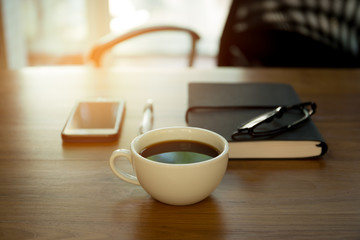 Cup of coffee and note pad with pen and glasses on the wooden de