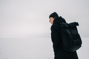 back young man with a black backpack, traveling on snow-covered winter places