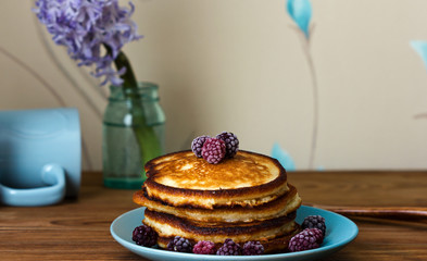 Homemade fluffy pancakes with fresh berries on a blue plate on a wooden table.