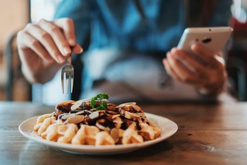 Hand of woman having breakfast and using on a mobile phone.