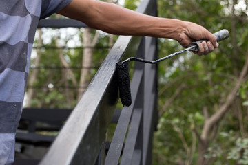 Hand holding paint roller applying black paint on metal stair