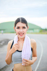 Young woman wearing sports clothes and towels, sport women listening to music with headphones in the stadium, is smiling and happy