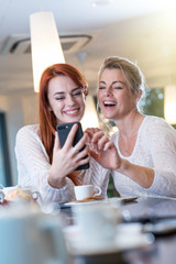  a mother and her daughter sit in a cafe using a phone