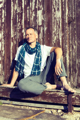 Man wearing in scarf sits on the porch of an old wooden hut