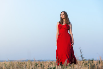 Obraz premium Gorgeous young woman in red dress walking in golden field