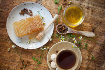 Serving table: drawn honey comb with honey dipper on a ceramic plate with cup of black tea.