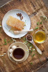 Serving table: drawn honey comb with honey dipper on a ceramic plate with cup of black tea.