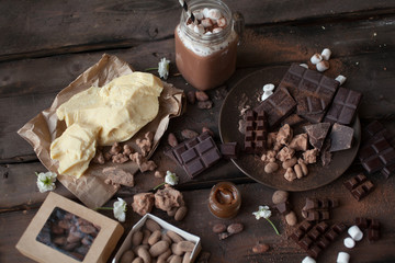 Serving table: pieces of parmesan cheese and chocolate with cacao on the wooden background.